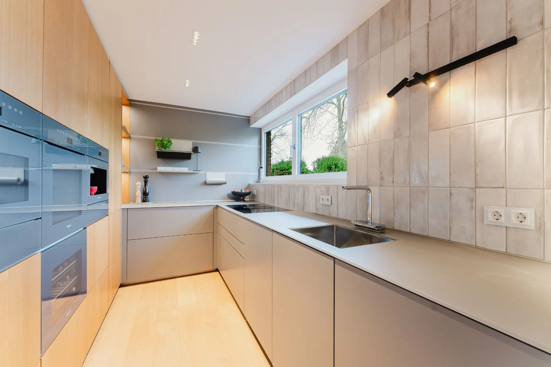 Moderne Küche mit grauen Schränken, Holzverkleidung, großem Fenster und integriertem Backofen.