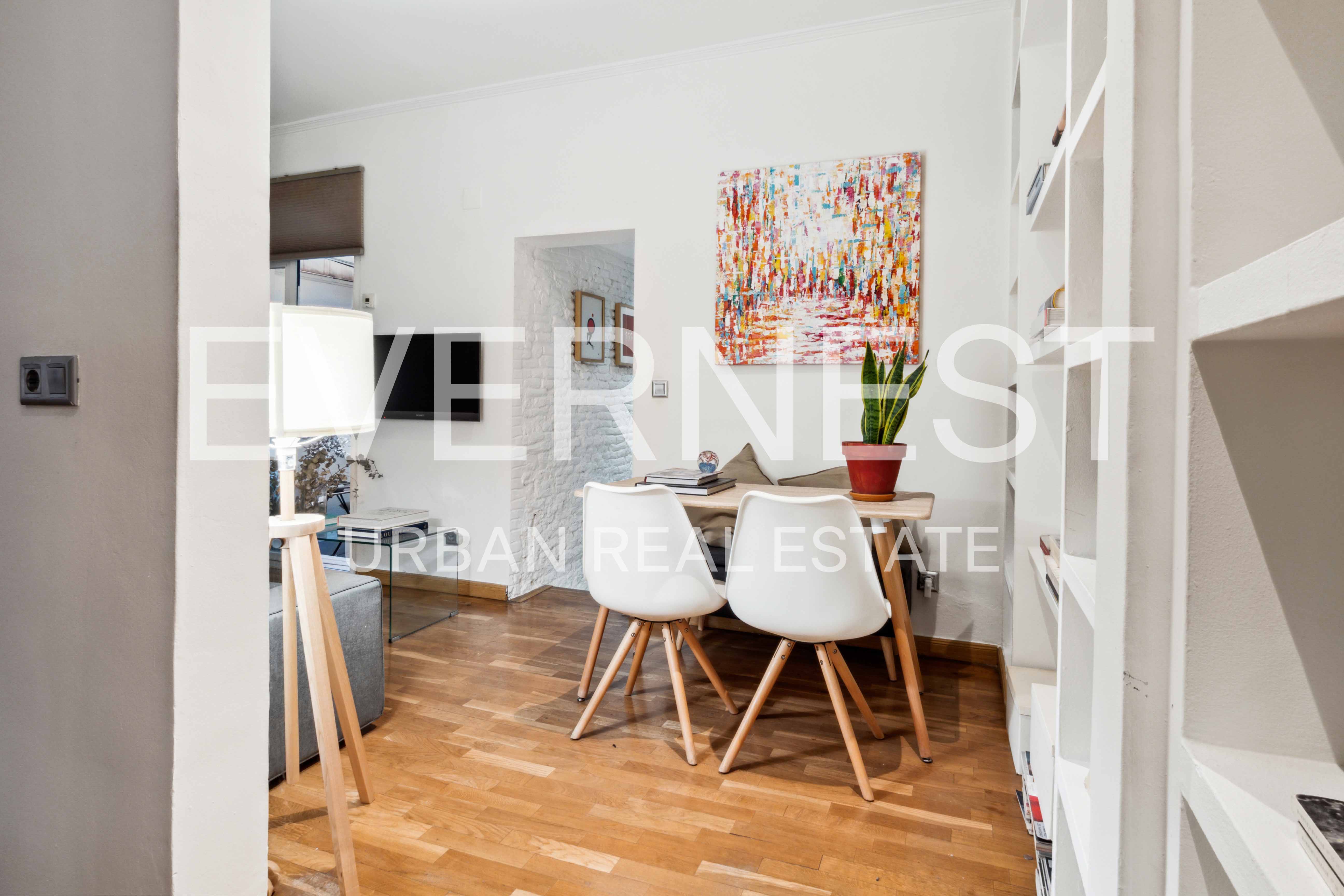 Essbereich mit Holztisch, weißen Stühlen, Pflanze und farbigem Bild an der Wand.