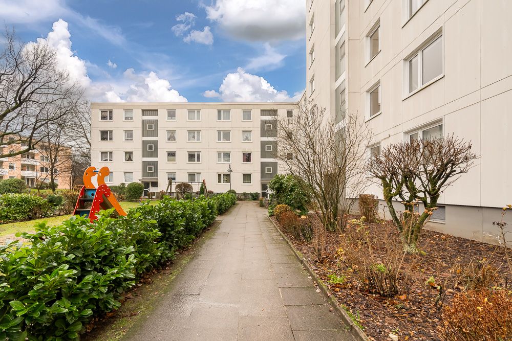 Gepflegter Weg zwischen Wohnhäusern mit Sträuchern und einem kleinen Spielplatz mit Rutsche.
