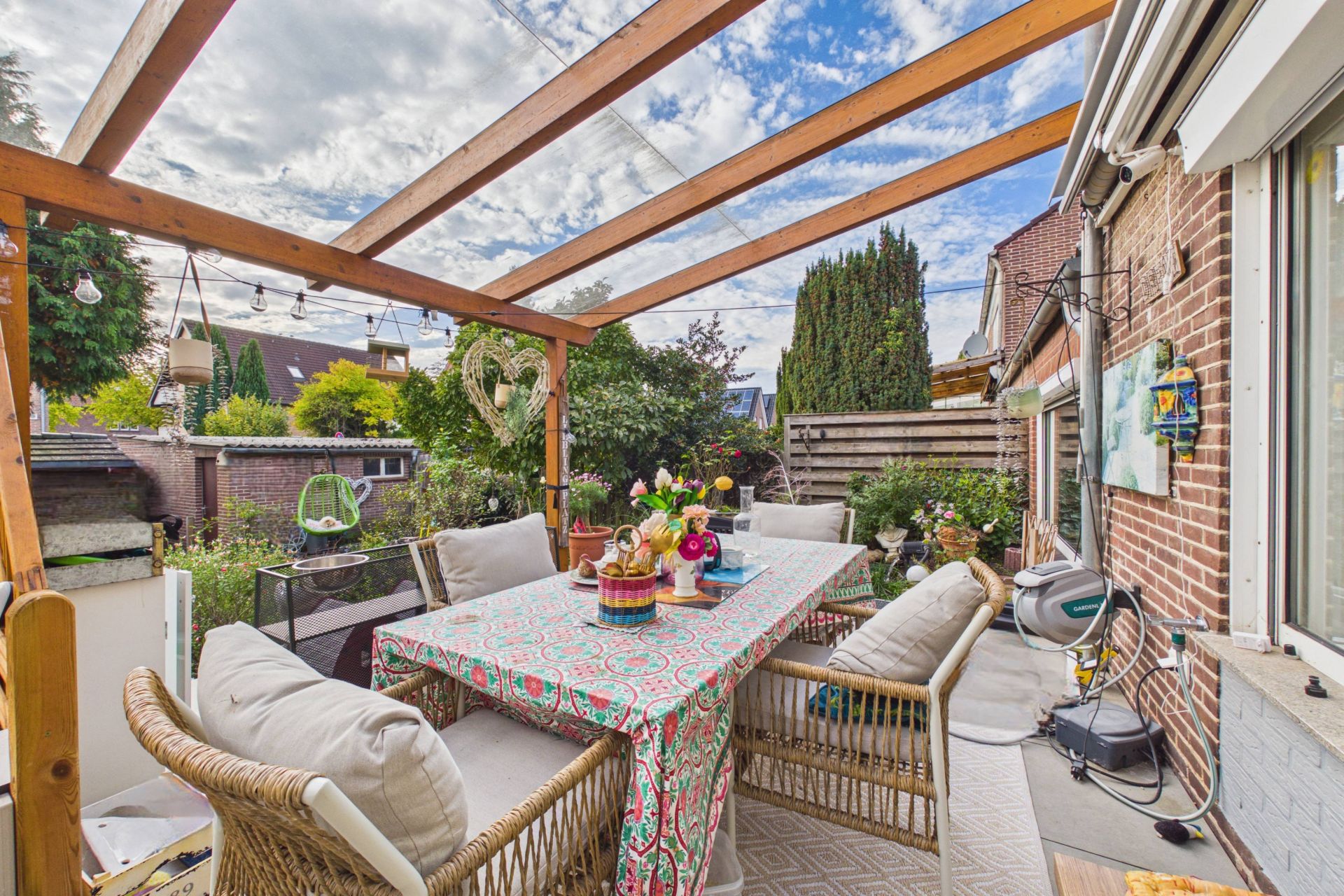 Überdachte Terrasse mit Esstisch, Stühlen und Pflanzen im Garten eines Wohnhauses.