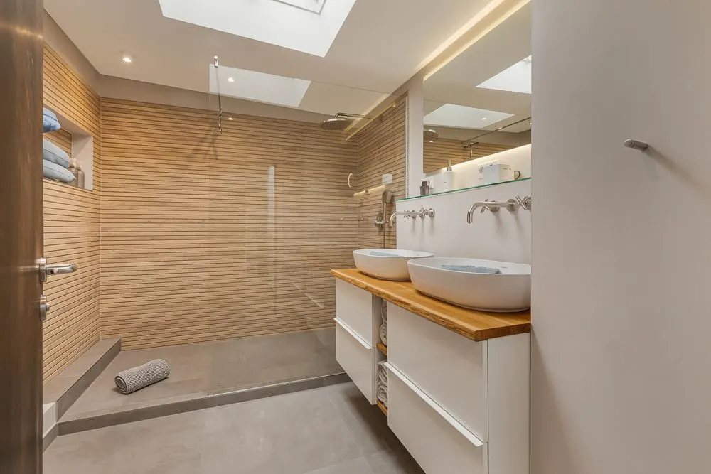 Modernes Badezimmer mit Holzakzenten, zwei Waschbecken und einer begehbaren Dusche.