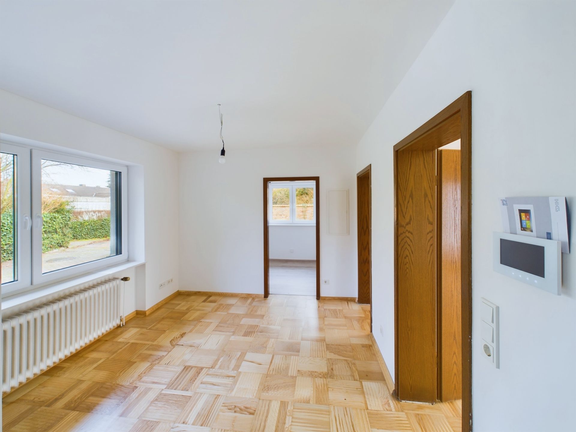 Helles Zimmer mit Parkettboden, großem Fenster, Heizkörper und mehreren Türen.