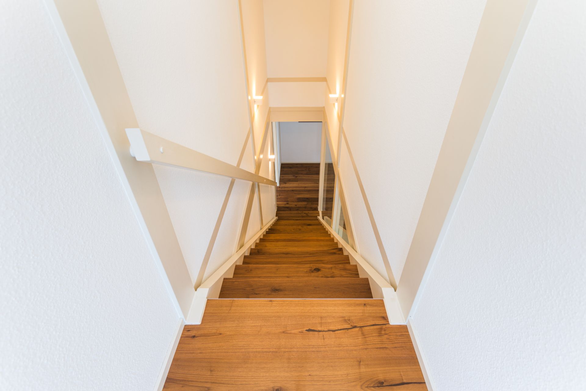 Holztreppe mit Handlauf, führt in einen Flur mit Holzboden.