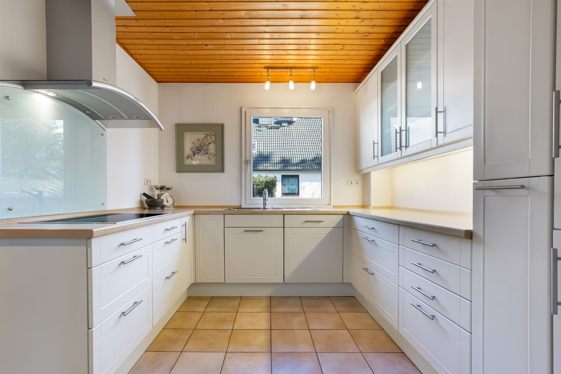 Helle, moderne Küche mit weißen Schränken, Holzdecke und Fenster über der Spüle.