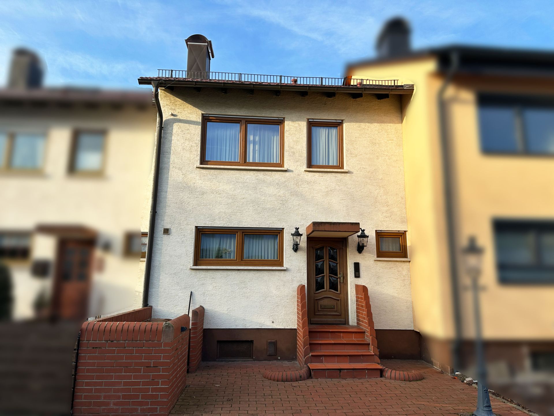 Zweistöckiges Wohnhaus mit braunen Fenstern, brauner Tür und kleiner Eingangstreppe aus Backstein.
