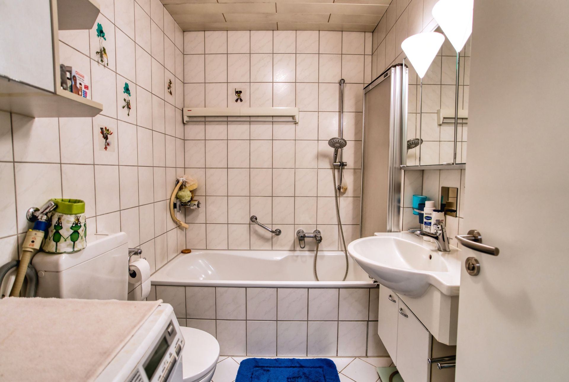 Kleines Badezimmer mit Badewanne, Waschbecken, Spiegel und Waschmaschine.