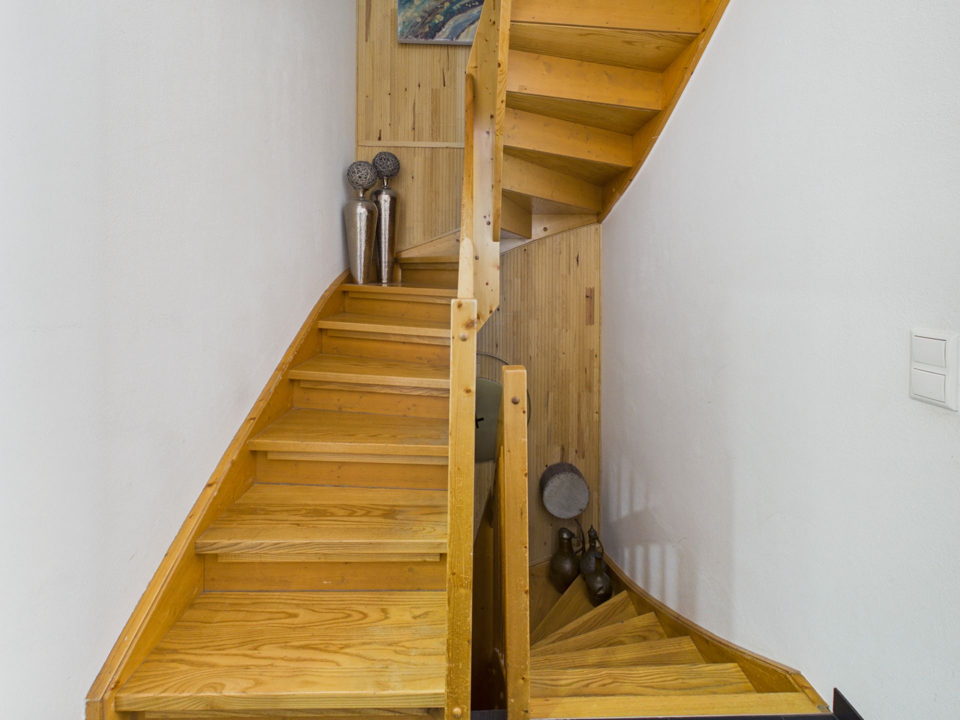 Holztreppe mit Dekovasen und Wandbild in einem Wohnhaus.