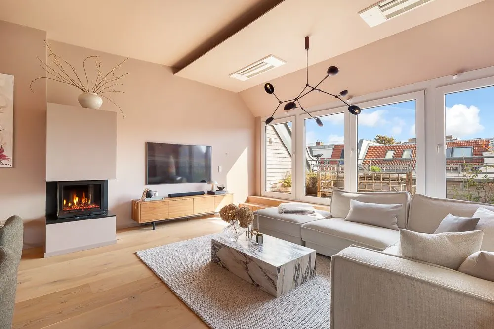 Helles Wohnzimmer mit Kamin, großen Fenstern, Sofa, Couchtisch und TV.