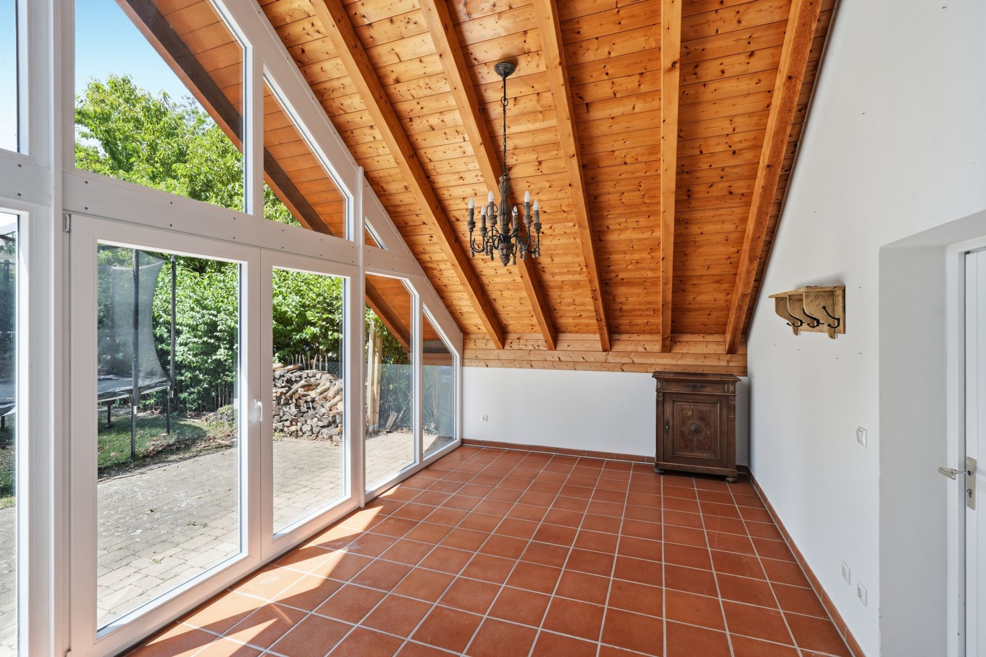 Heller Raum mit Terrakotta-Fliesen, Holzdecke und großen Fenstern, Blick in den Garten.