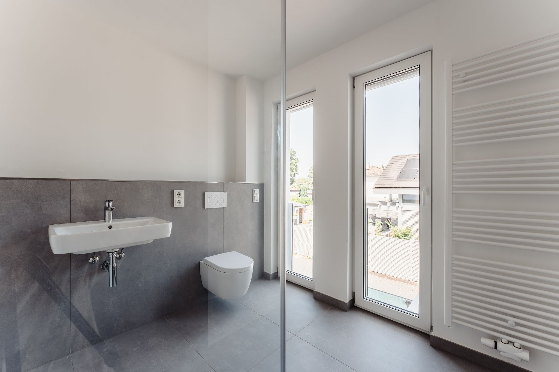 Modernes Badezimmer mit Wandwaschbecken, Hänge-WC, Fenster und Handtuchheizkörper.