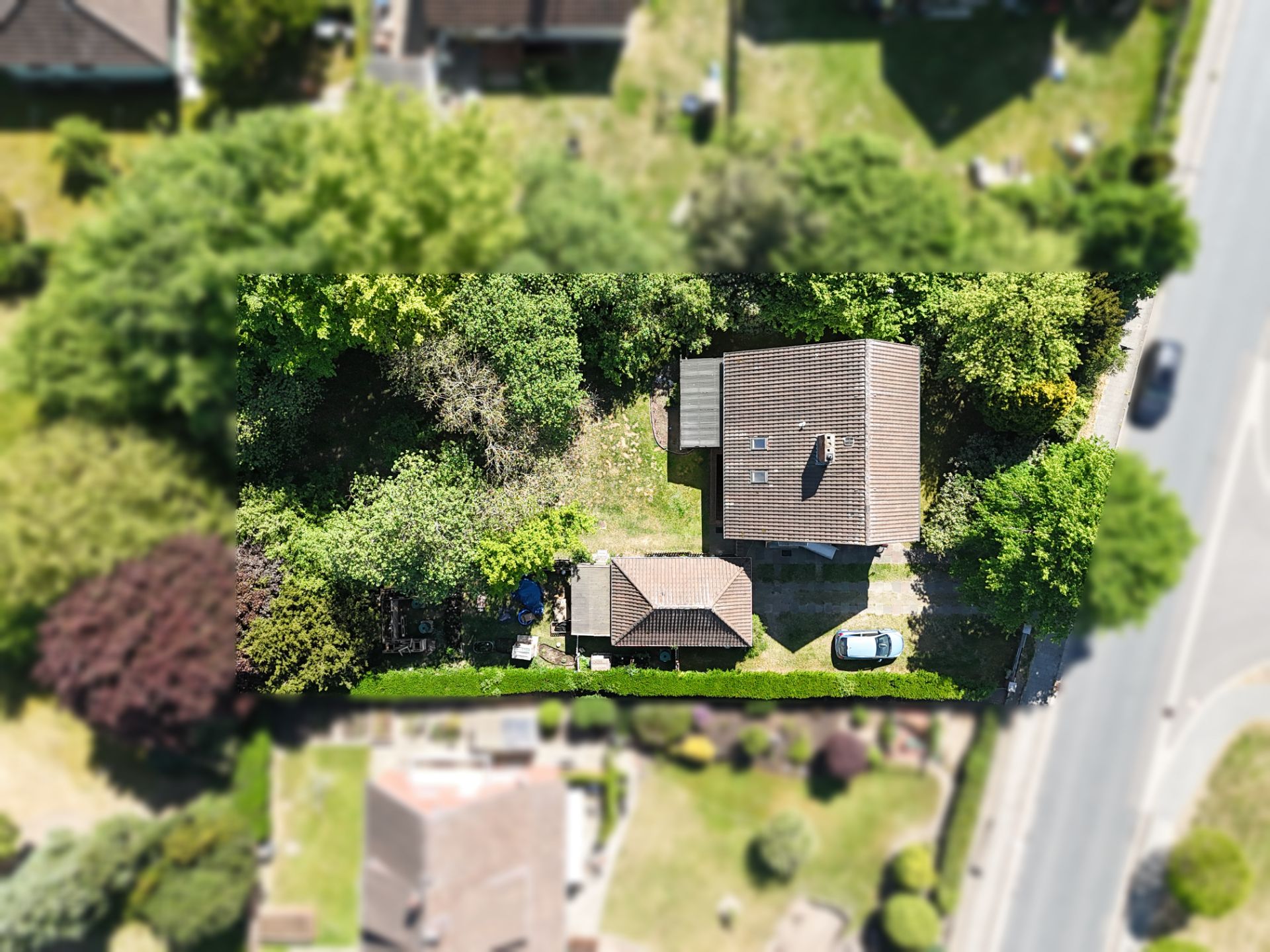 Luftaufnahme eines Wohnhauses mit Nebengebäude, Garten und Auto in einer grünen Umgebung.