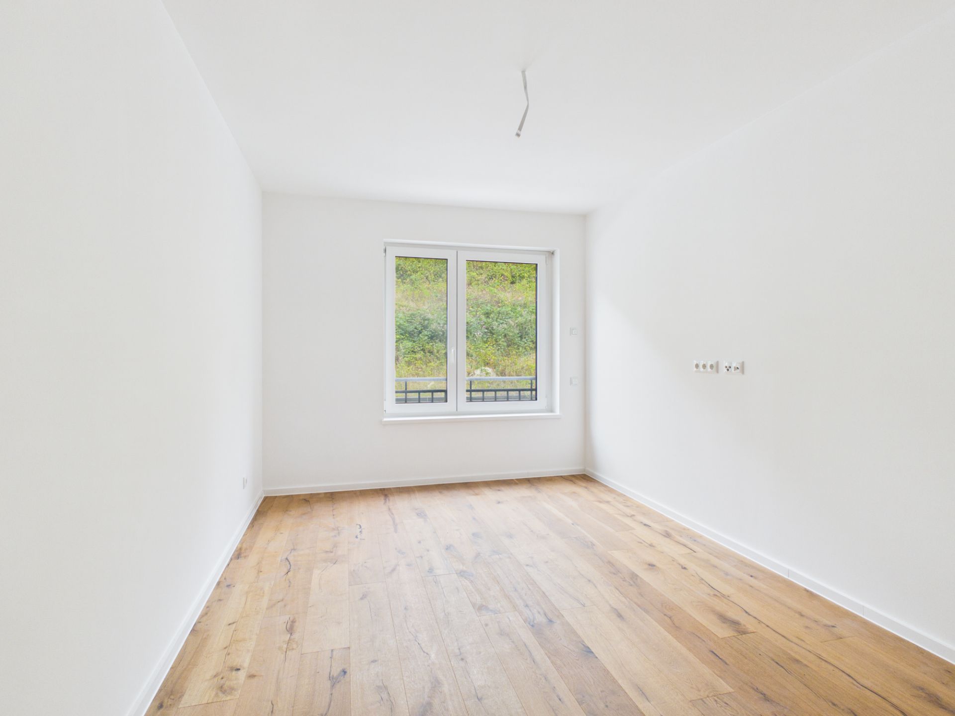 Leerer, heller Raum mit Holzfußboden und großem Fenster.