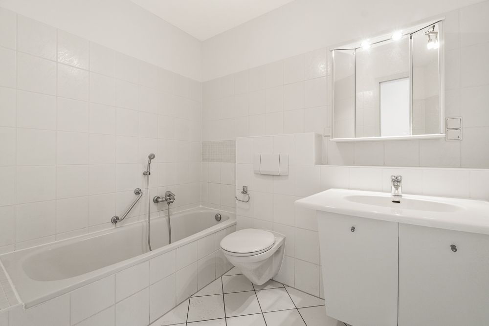 Helles Badezimmer mit Badewanne, Wandtoilette, Waschbecken und Spiegelschrank.