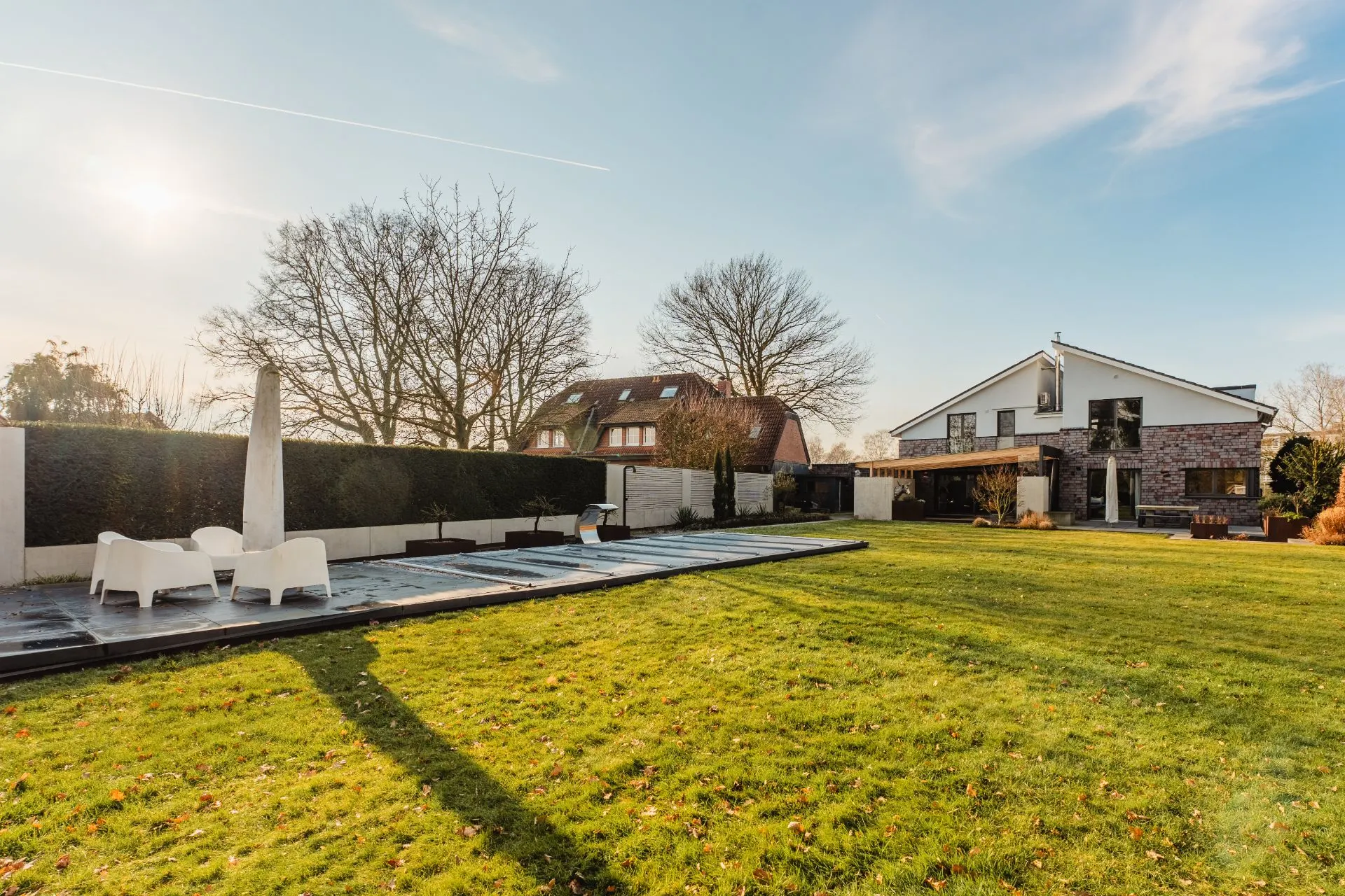 Großer Garten mit Rasen, Poolabdeckung, Sitzgruppe und modernem Wohnhaus im Hintergrund.