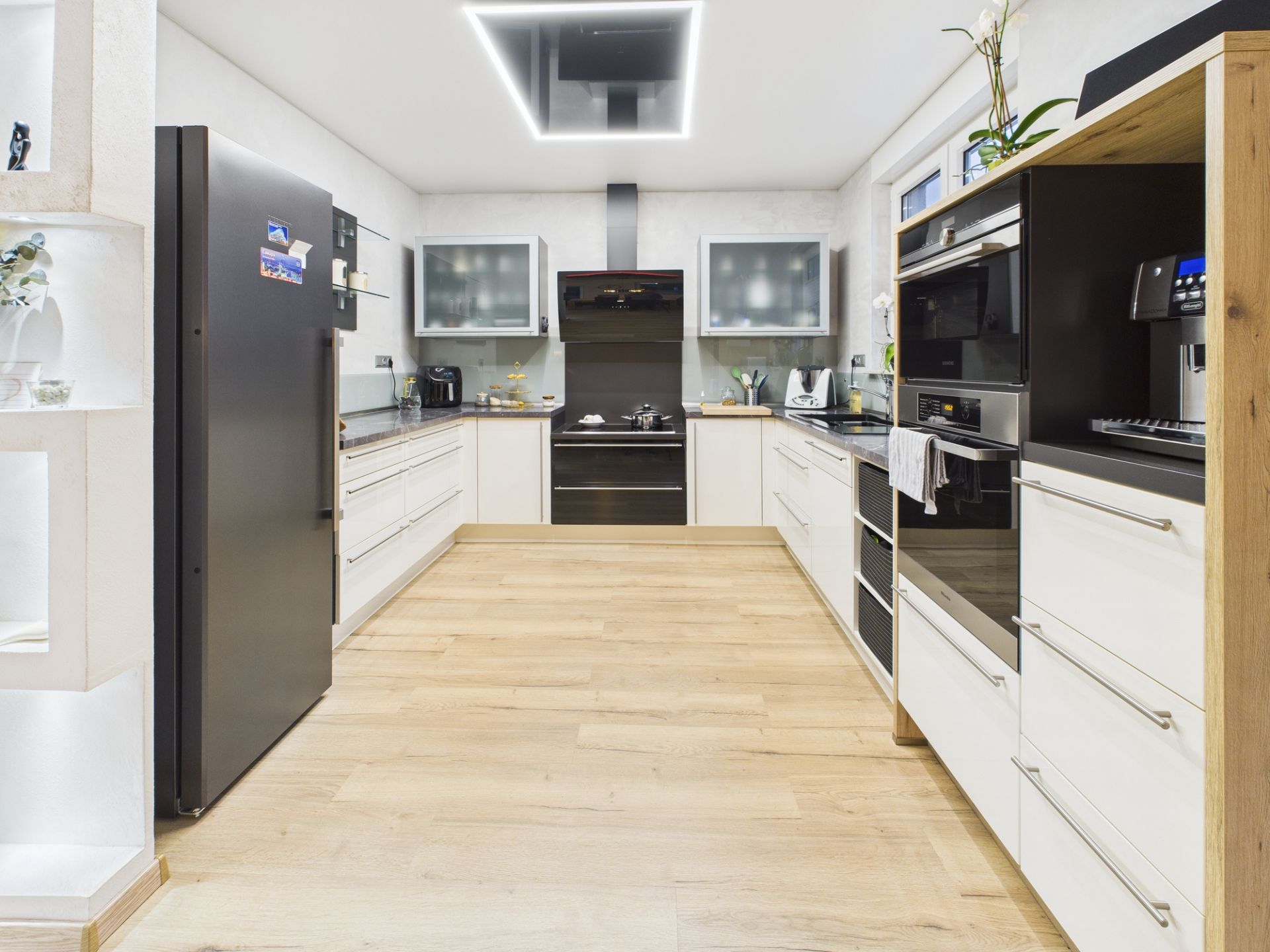 Moderne Küche mit weißen Schränken, Holzfußboden und Edelstahlgeräten.