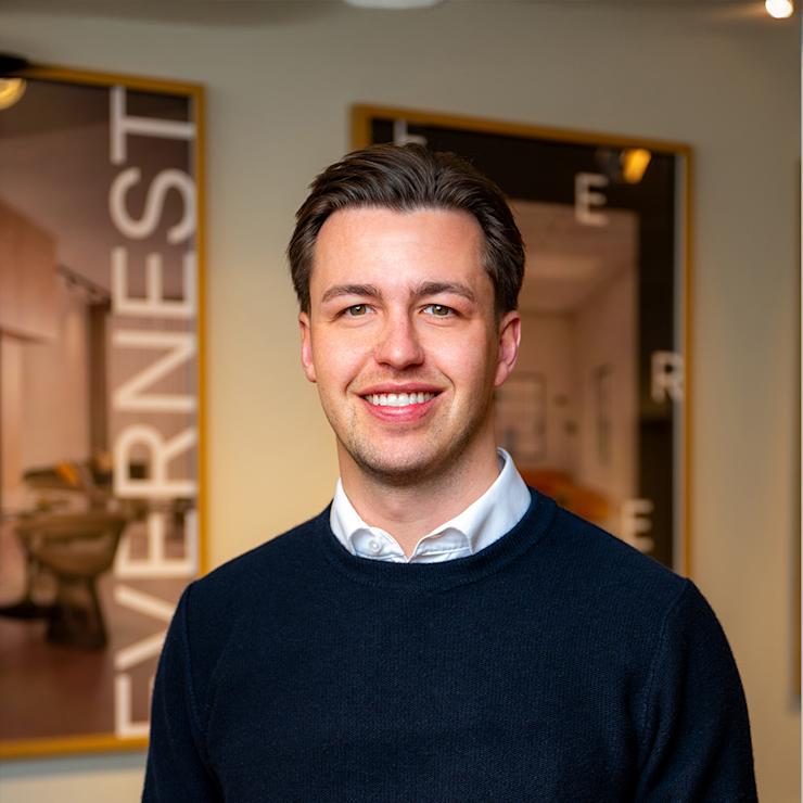 Ein Mann mit dunklem Pullover steht in einem hellen Raum mit gerahmten Bildern an der Wand.