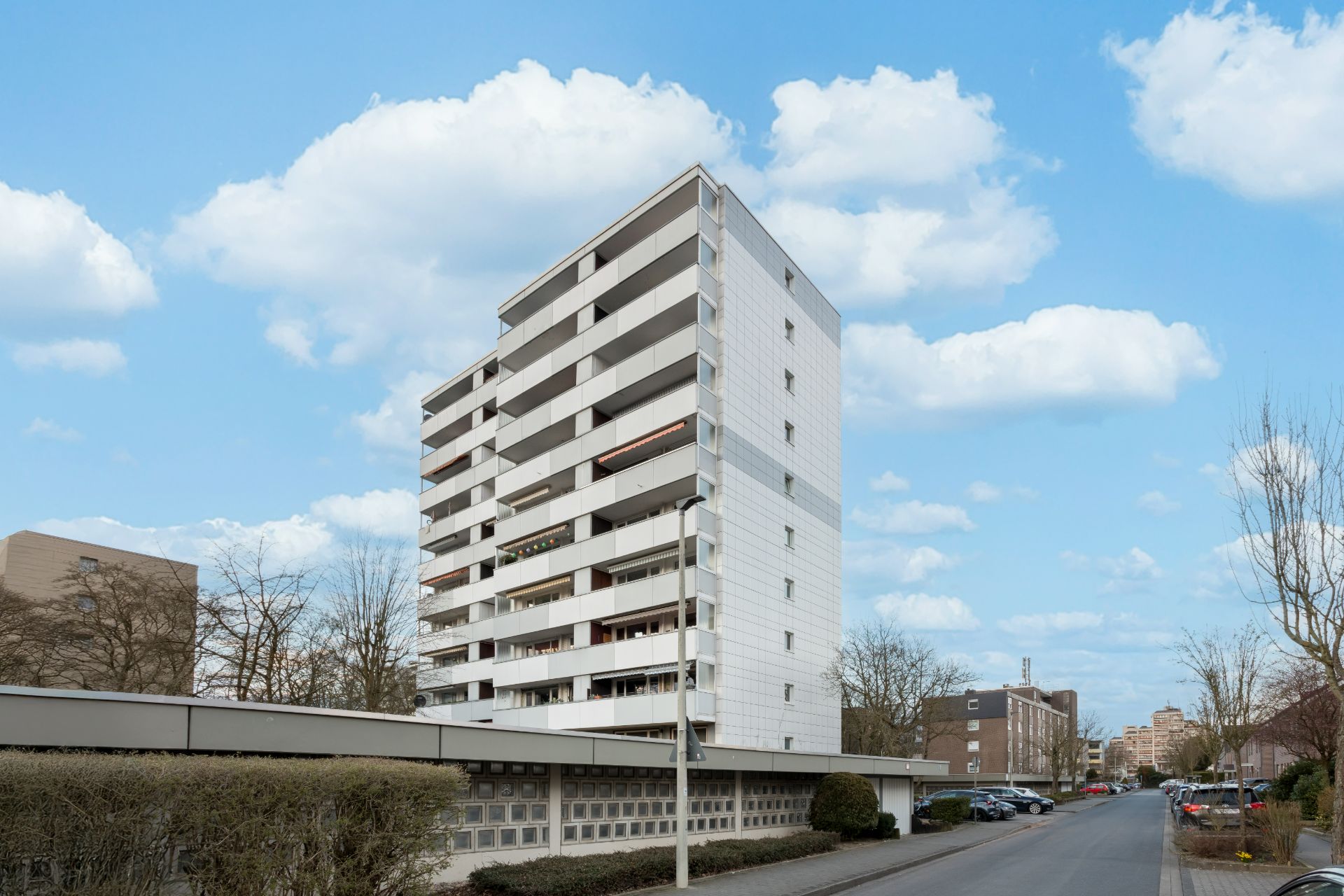 Mehrstöckiges Wohnhaus mit Balkonen an einer ruhigen Straße bei Tageslicht.