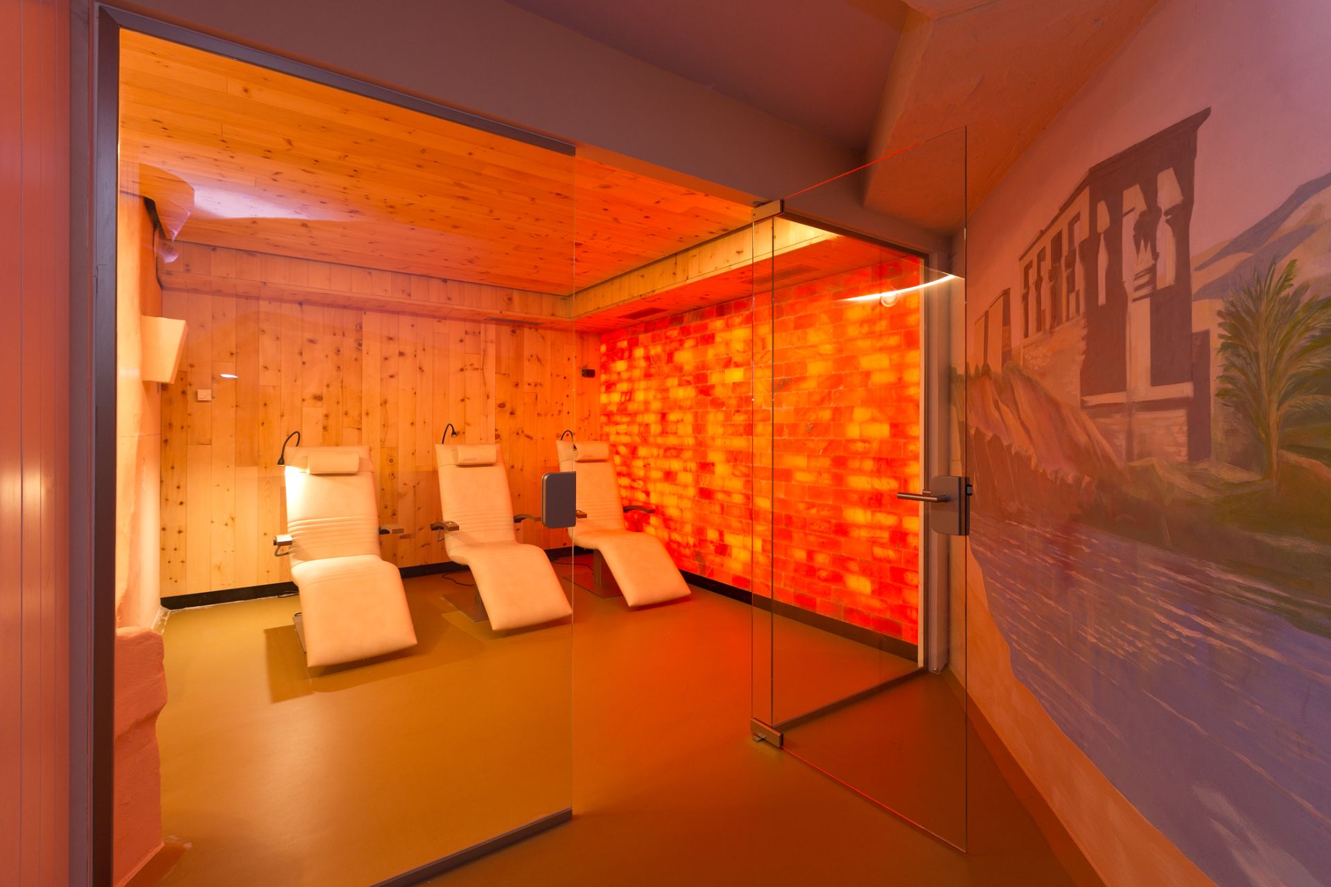 Raum mit drei Liegestühlen, Holzwänden und orange beleuchteter Wand aus Salzsteinen.