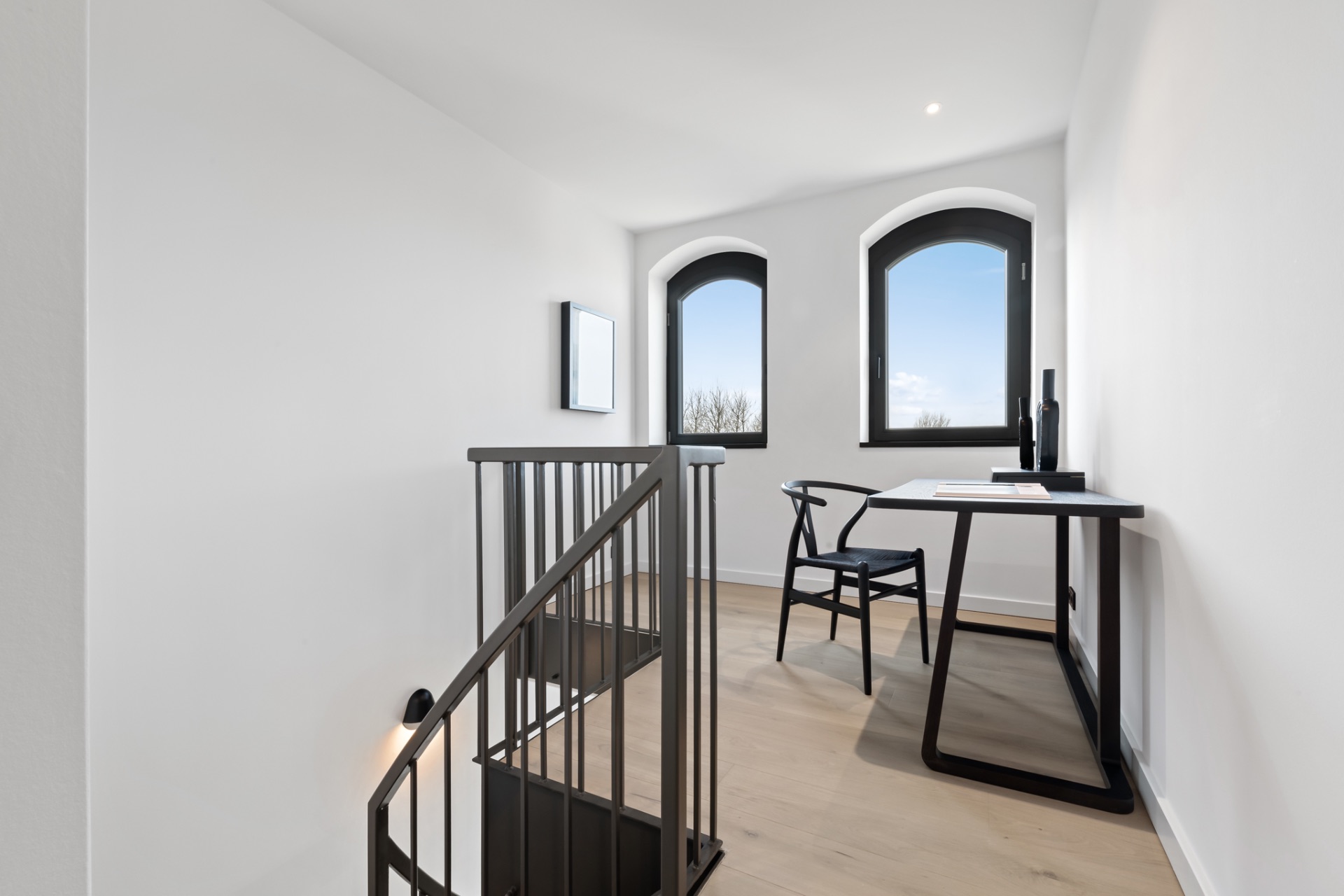 Heller Raum mit Wendeltreppe, zwei Fenstern und einem Schreibtisch mit Stuhl.