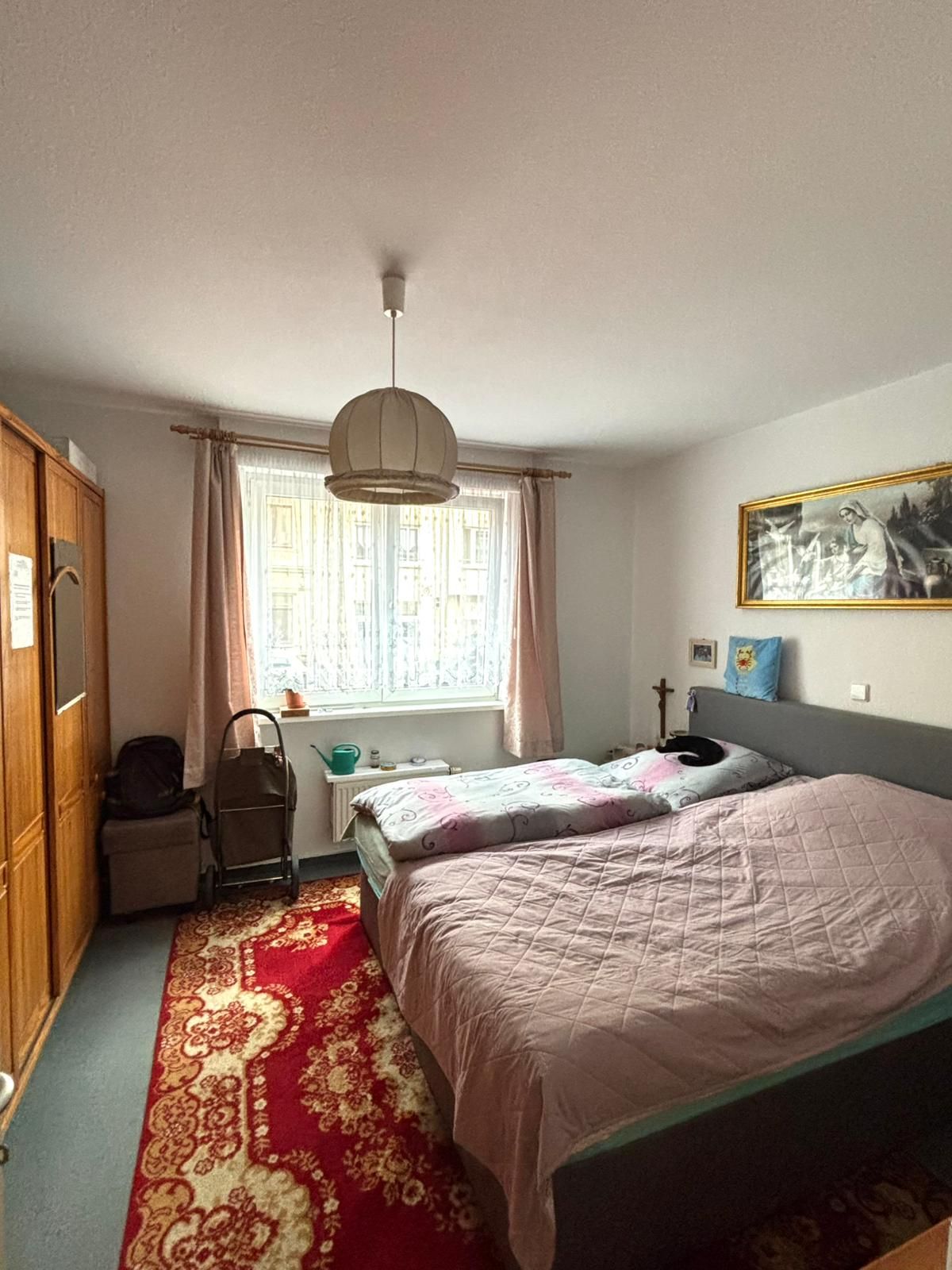 Schlafzimmer mit Doppelbett, großem Fenster, Teppich, Schrank und Deckenlampe.