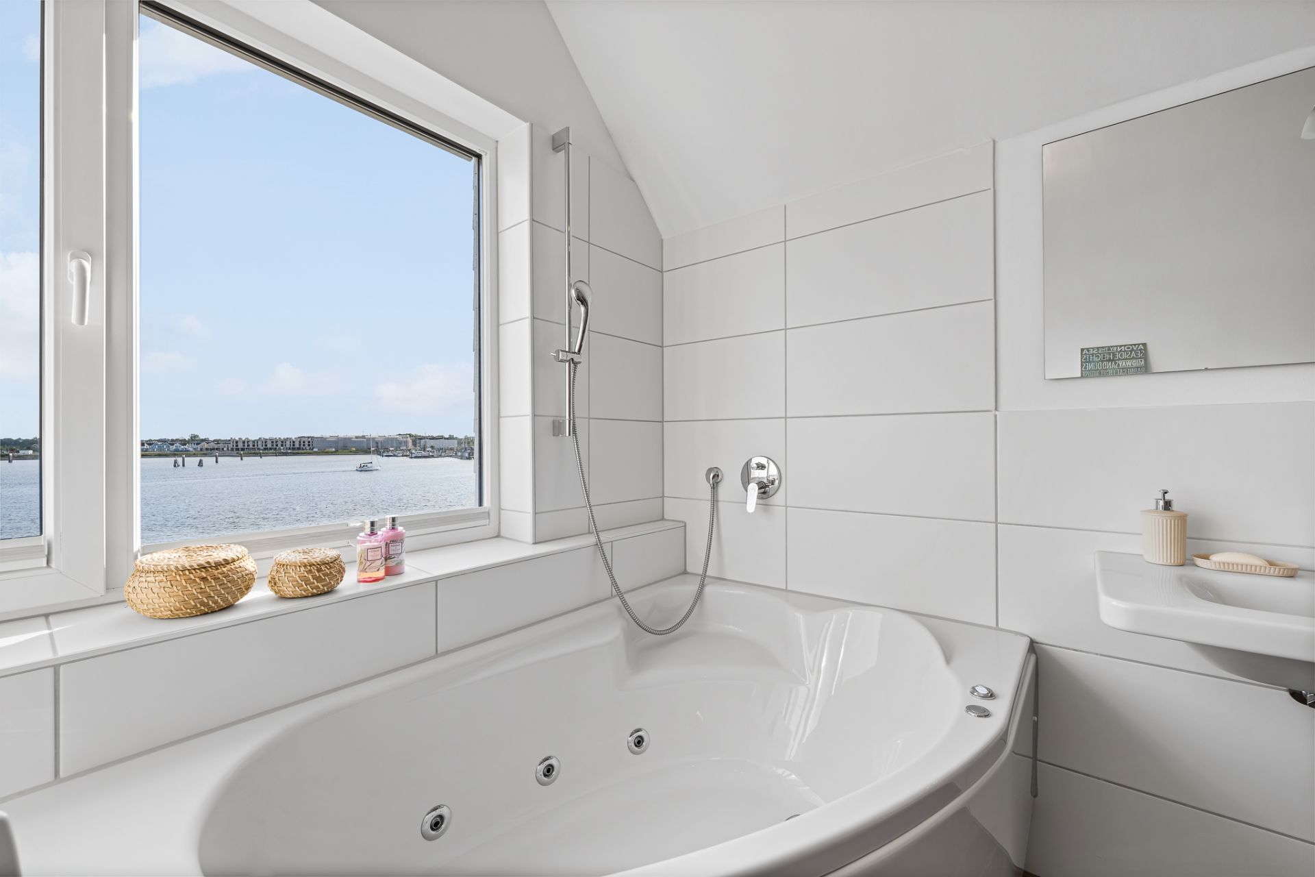 Helles Bad mit großer Eckbadewanne, Fenster mit Seeblick und weißen Fliesen.