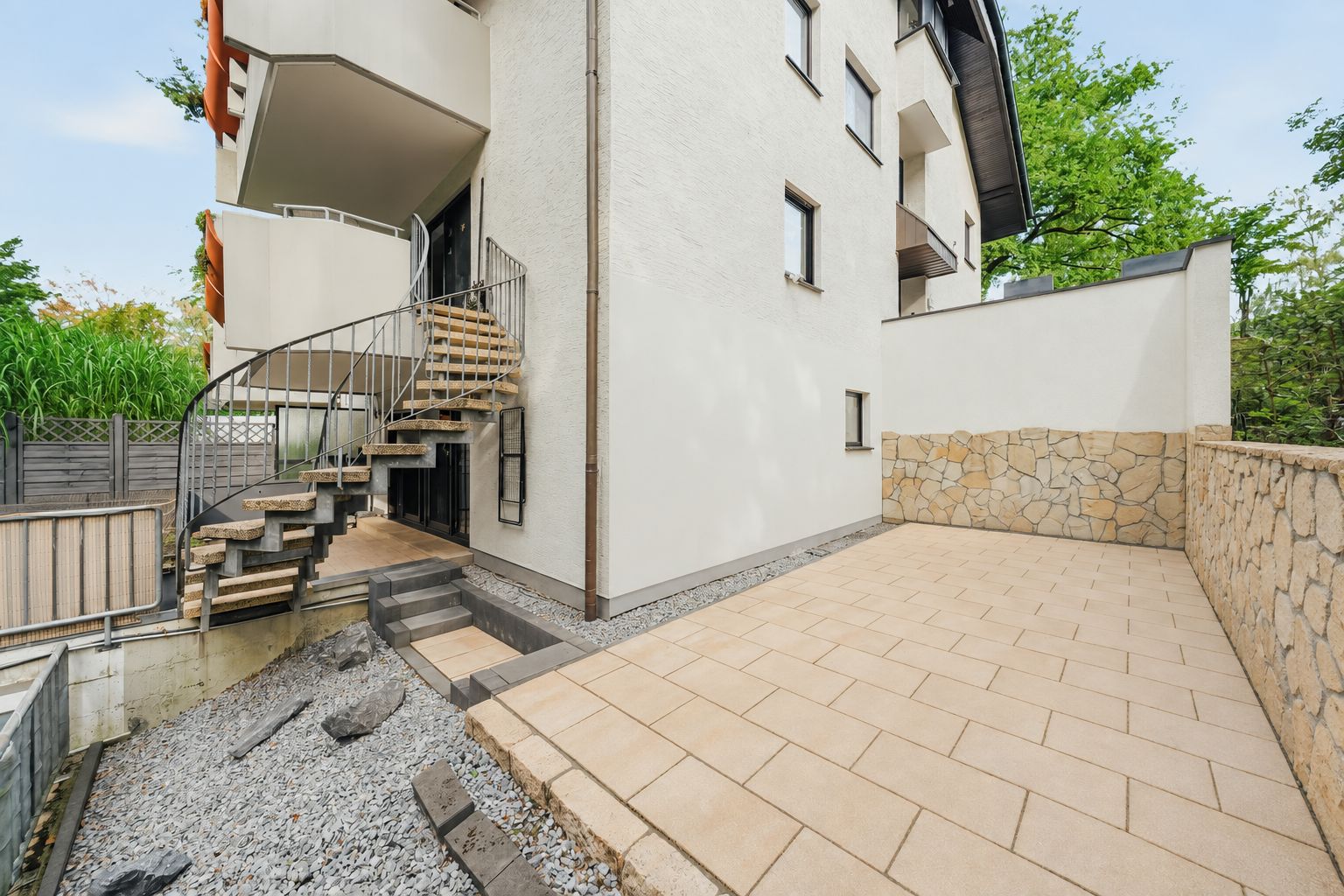 Gepflasterte Terrasse mit Steintreppe und Spiral-Außentreppe an einem Wohnhaus.