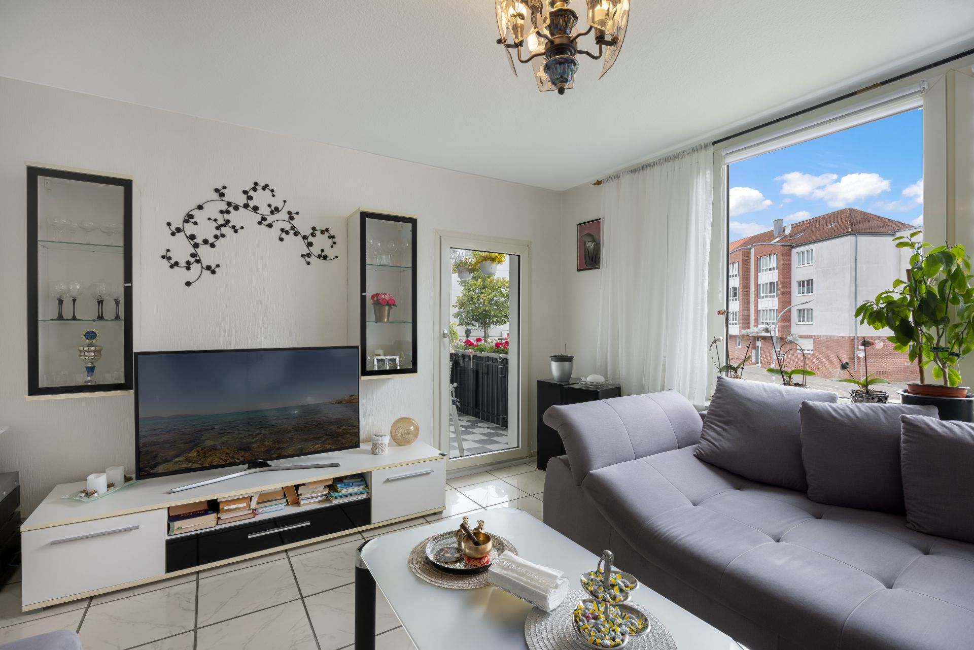 Helles Wohnzimmer mit grauem Sofa, Couchtisch, Fernseher und großen Fenstern mit Blick nach draußen.