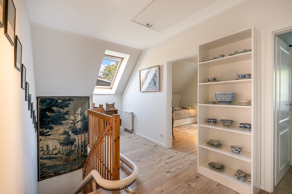 Heller Flur mit Treppe, Regal mit Geschirr und Zugang zu einem Schlafzimmer.