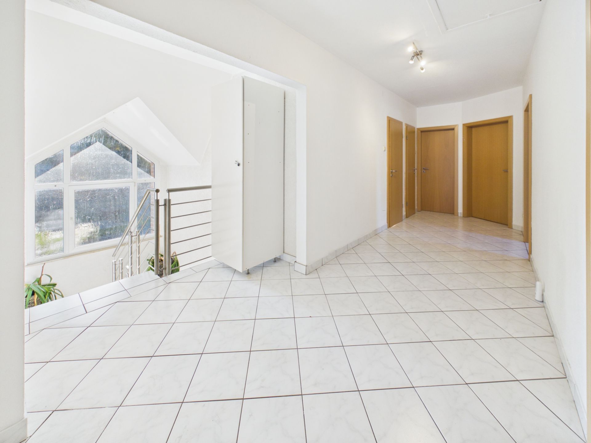 Heller Flur mit Fliesenboden, mehreren Holztüren und Treppe mit großem Fenster.