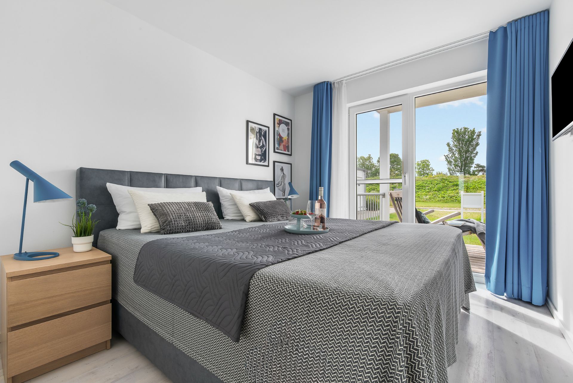 Helles Schlafzimmer mit Doppelbett, Nachttisch, blauer Lampe und Zugang zur Terrasse.