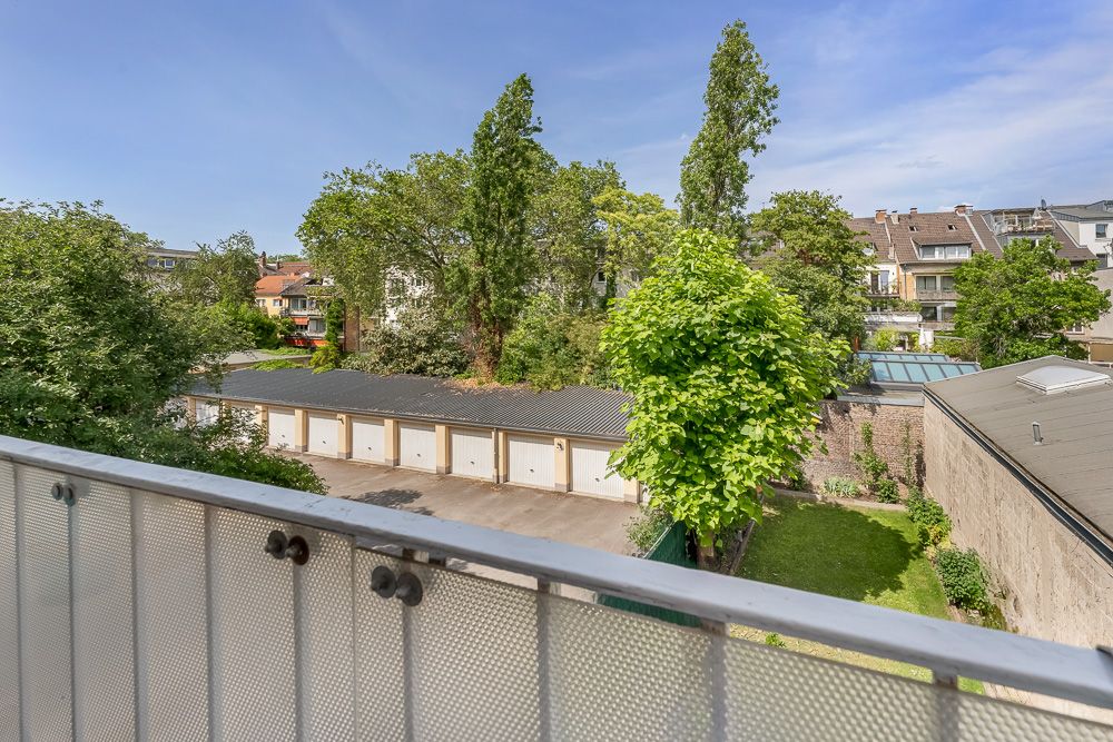 Blick von einem Balkon auf Garagen, Bäume und Nachbarhäuser bei sonnigem Wetter.