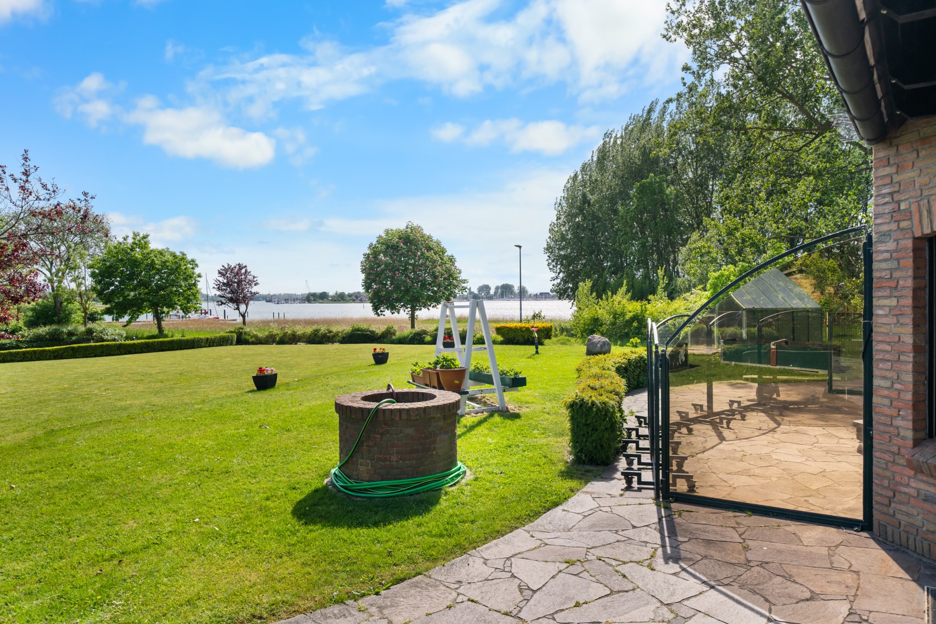 Großer Garten mit Rasen, Brunnen, Schaukel und Terrasse neben einem Backsteinhaus.