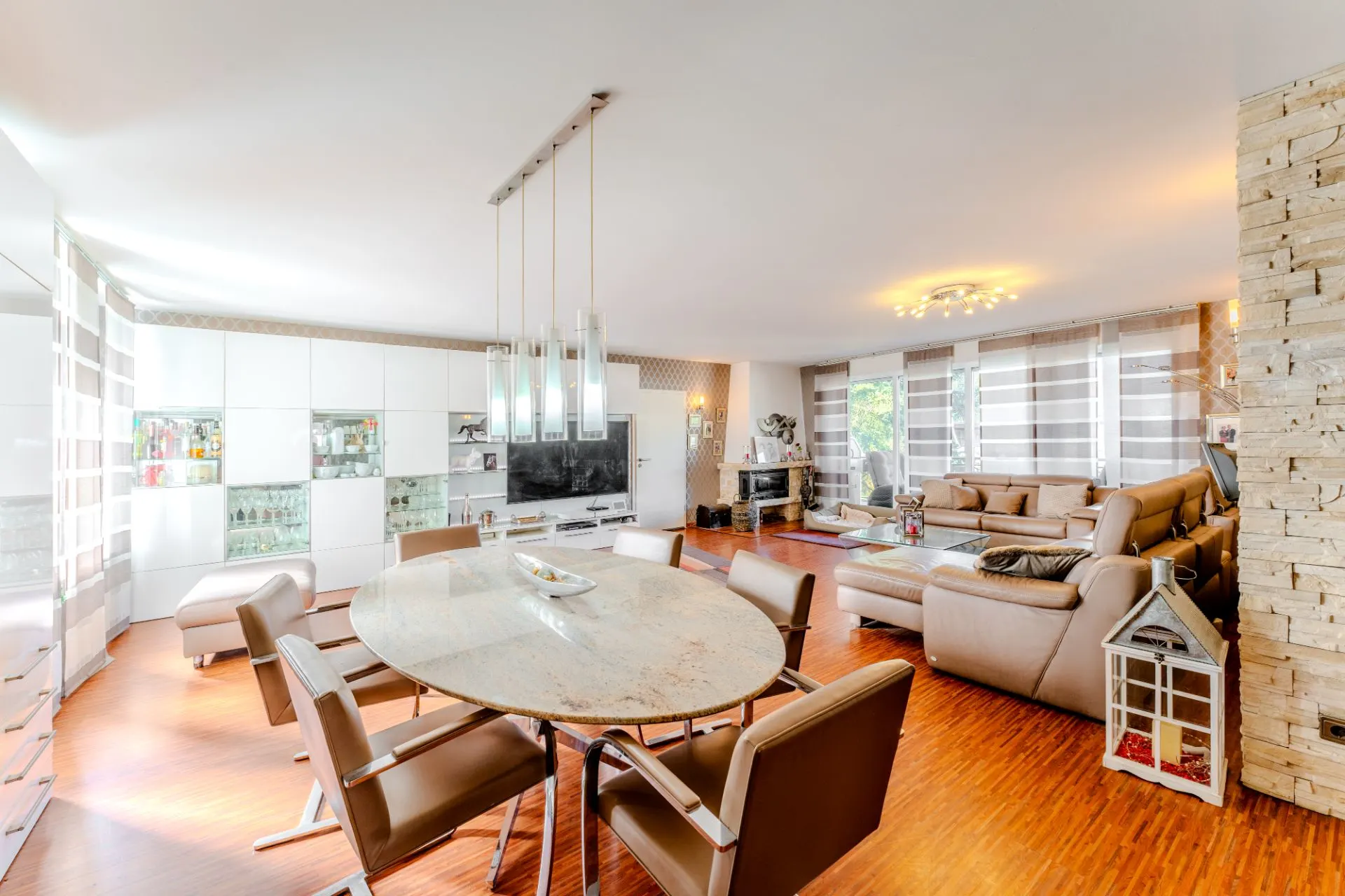 Modernes Wohnzimmer mit großem Sofa, Esstisch, Fernseher und großen Fenstern.