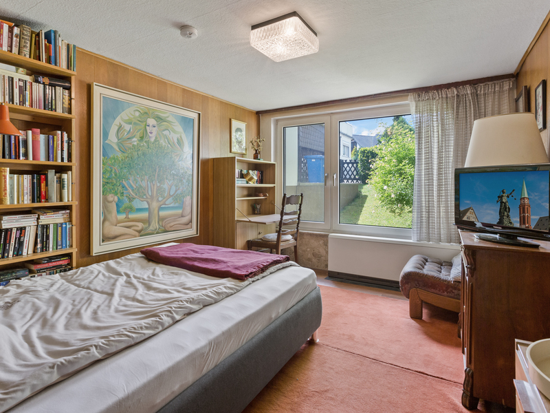 Schlafzimmer mit Bett, Bücherregal, großem Fenster, Schreibtisch und Fernseher.