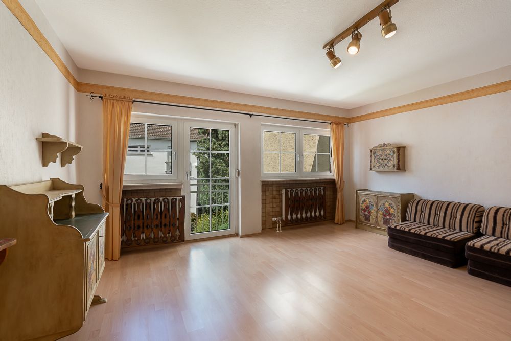 Helles Wohnzimmer mit Holzfußboden, Sofa, Schreibtisch und großen Fenstern mit Vorhängen.