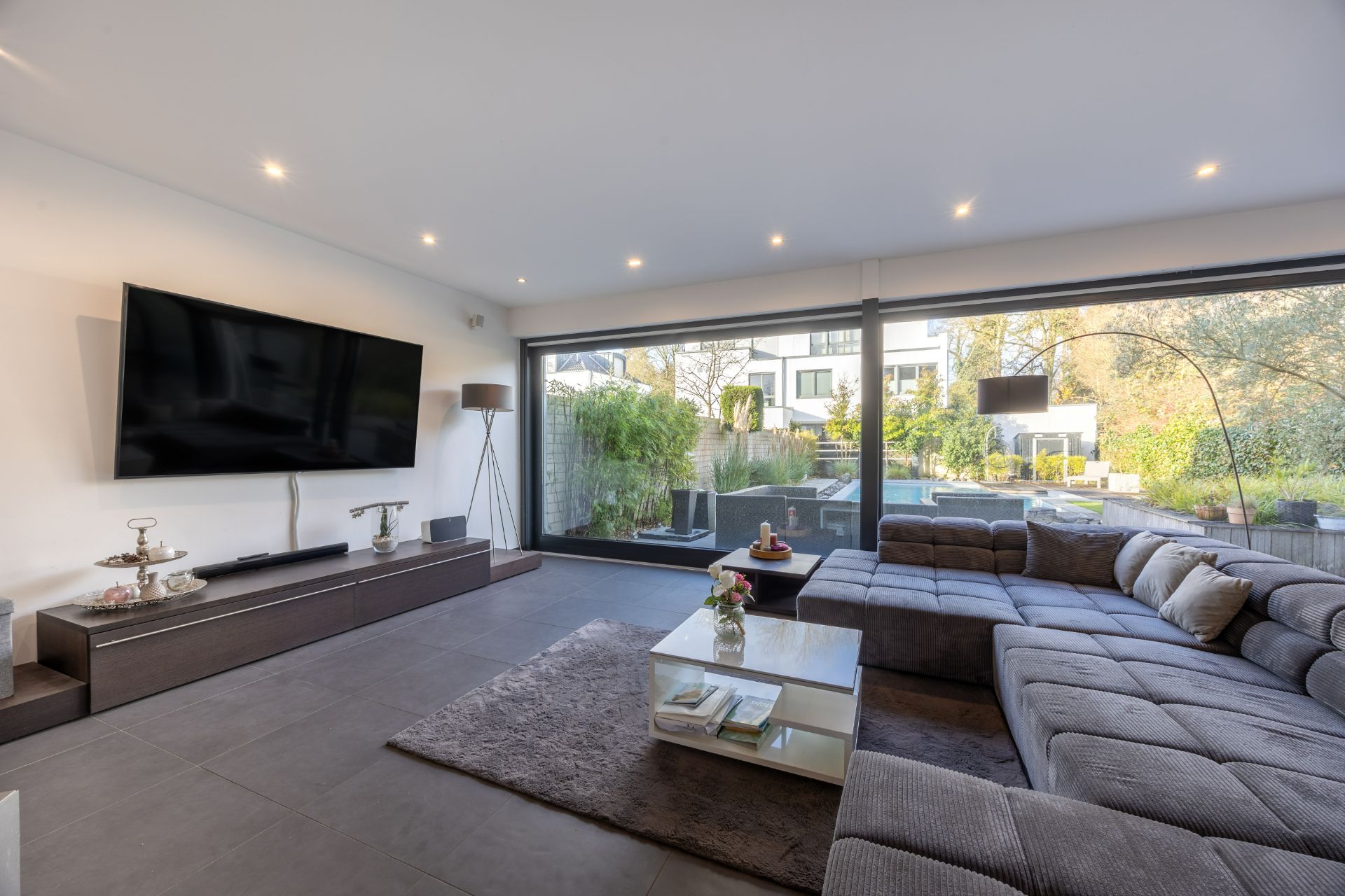 Modernes Wohnzimmer mit großem Sofa, Couchtisch, Fernseher und Blick auf die Terrasse durch große Fenster.