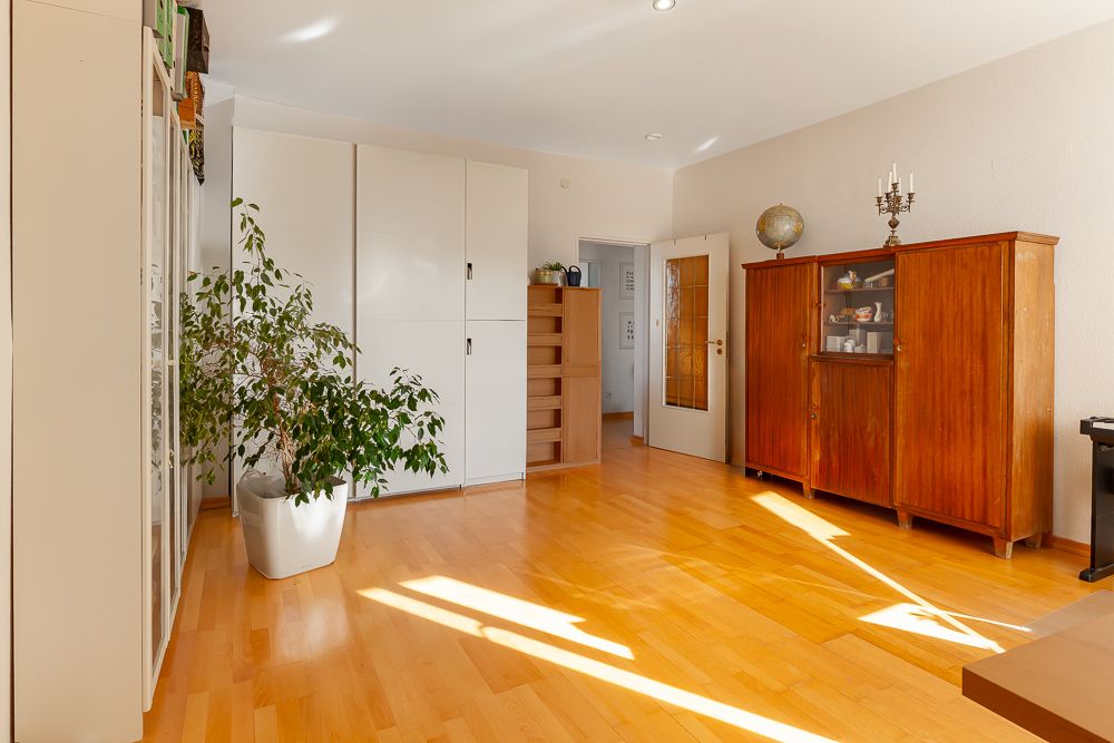 Helles Zimmer mit Holzschrank, weißen Schränken, Pflanze und Parkettboden.
