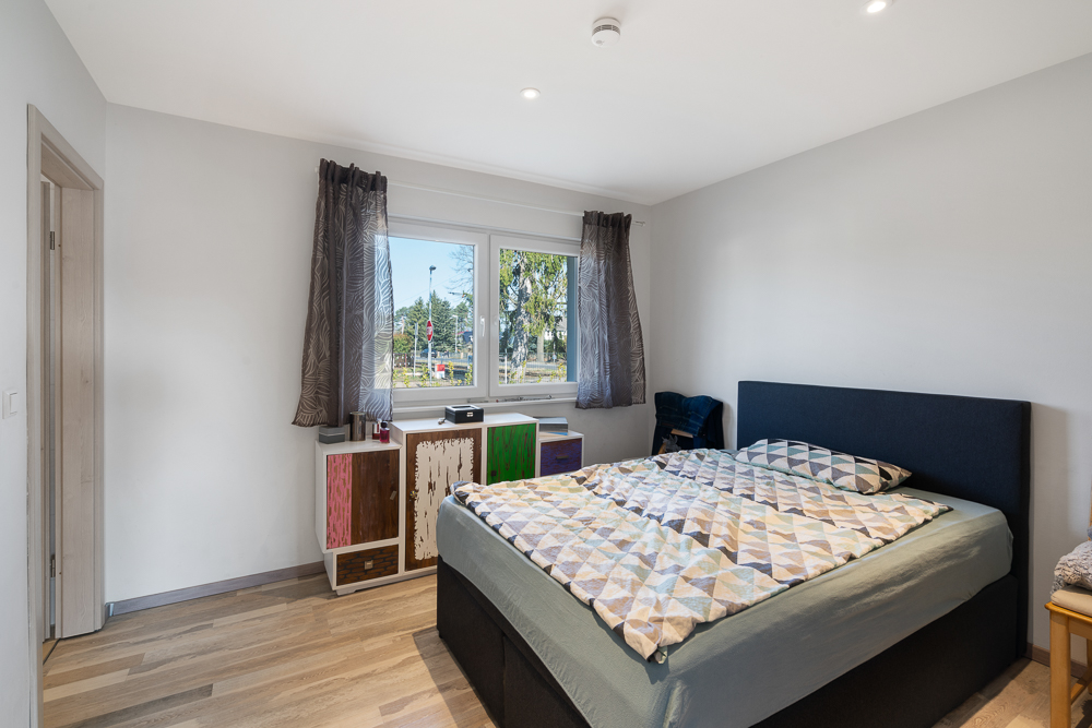 Modernes Schlafzimmer mit großem Bett, Kommode unter Fenster und Holzboden.