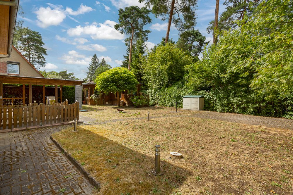 Garten mit Rasenfläche, Bäumen, einem Schuppen und gepflastertem Weg neben einem Wohnhaus.