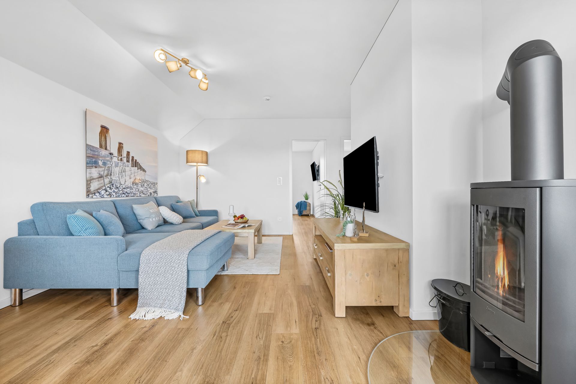 Modernes Wohnzimmer mit blauem Sofa, Holzboden, Kamin, TV und Wandbild.