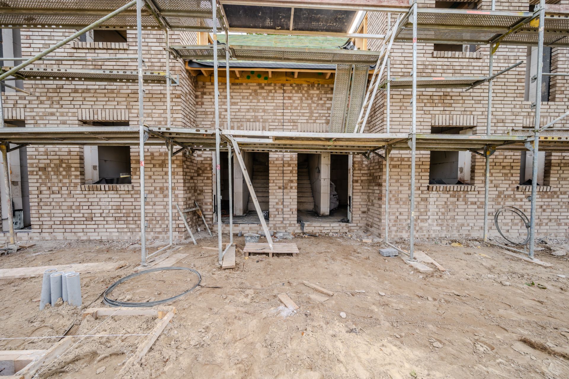 Backsteinwohnhaus im Bau mit Gerüst und offenen Fenstern, Erdarbeiten im Vordergrund.