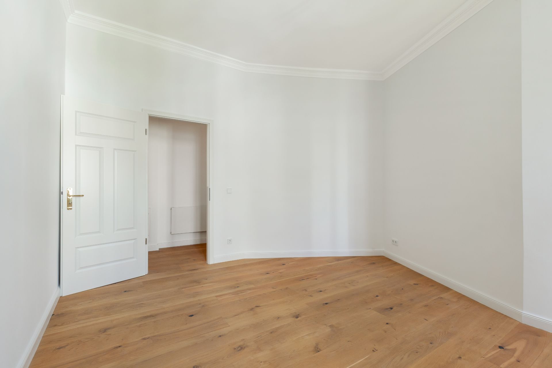 Leeres Zimmer mit Holzfußboden, weiß gestrichene Wände und geöffneter Tür.