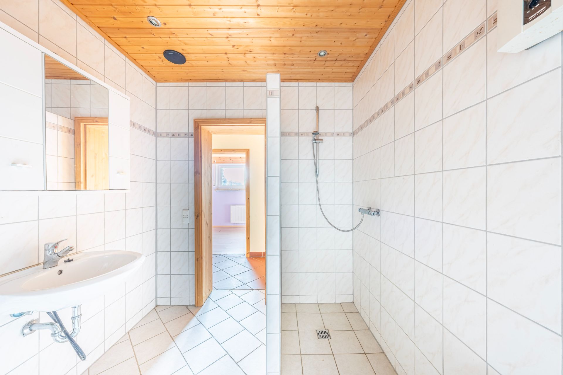 Helles Bad mit Waschbecken, Spiegel, offener Dusche und Holzbalkendecke.