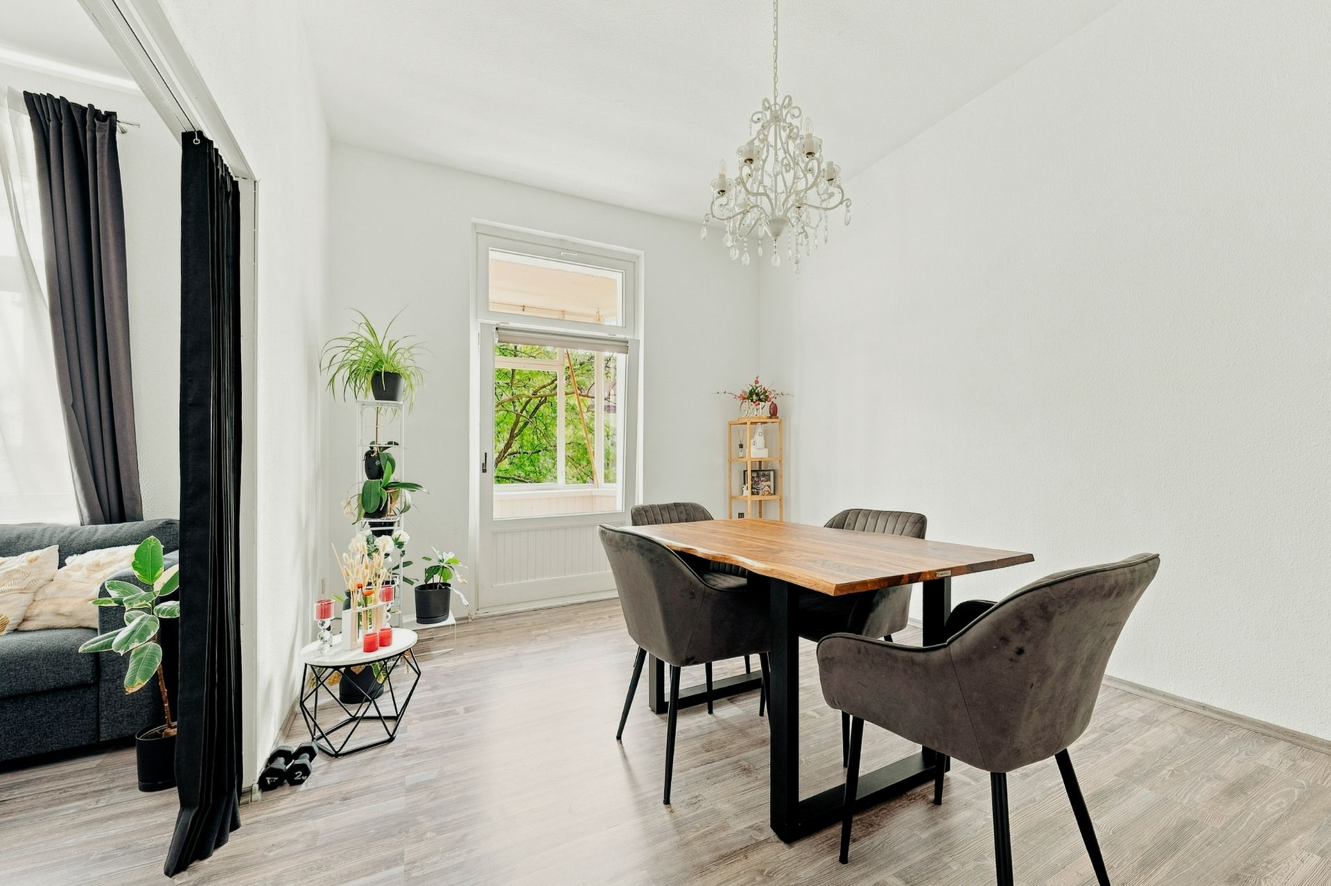 Esszimmer mit Holztisch, vier Stühlen, Kronleuchter und Fenster, angrenzendes Wohnzimmer sichtbar.