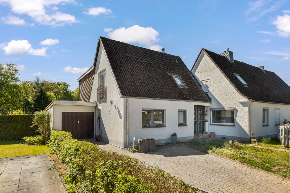 Doppelhaushälfte mit dunklem Satteldach, Garage und gepflasterter Einfahrt.