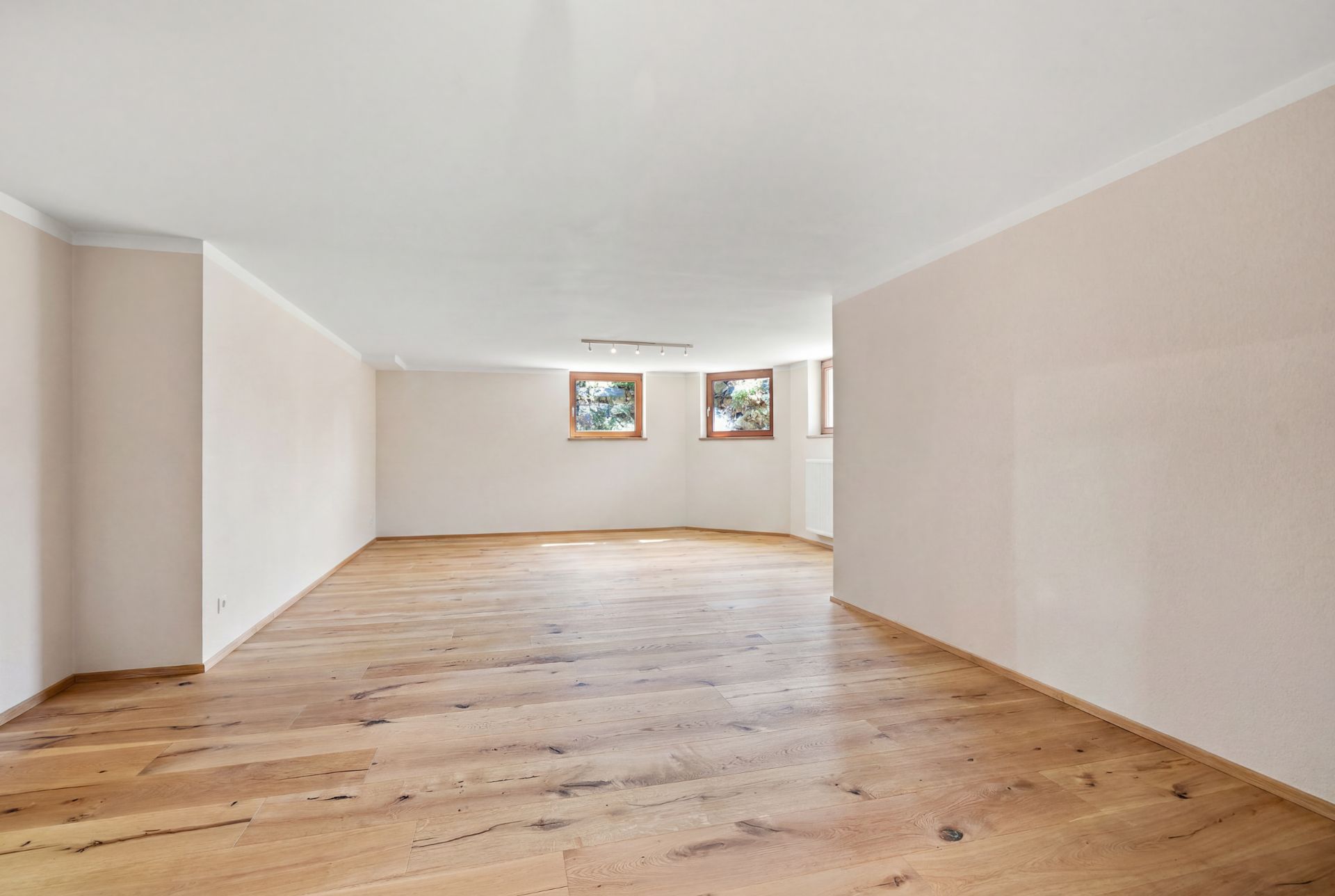 Heller, leerer Raum mit Holzfußboden und drei Fenstern an der Rückwand.