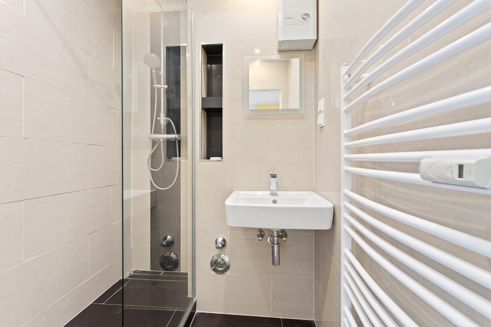 Modernes Badezimmer mit Dusche, Waschbecken, Spiegel und weißem Handtuchheizkörper.