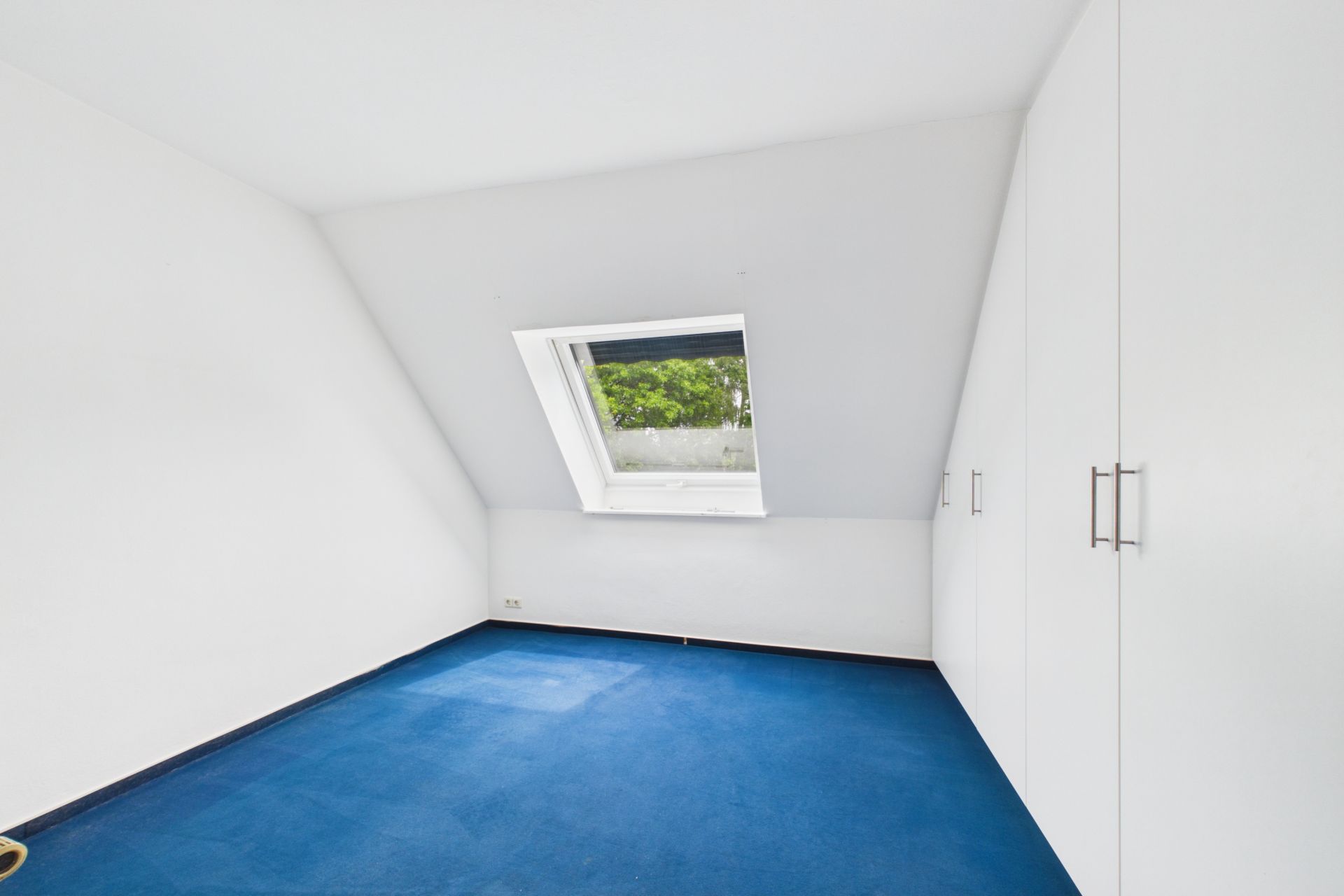Leerer Raum mit blauem Teppich, Dachfenster und weißen Einbauschränken.