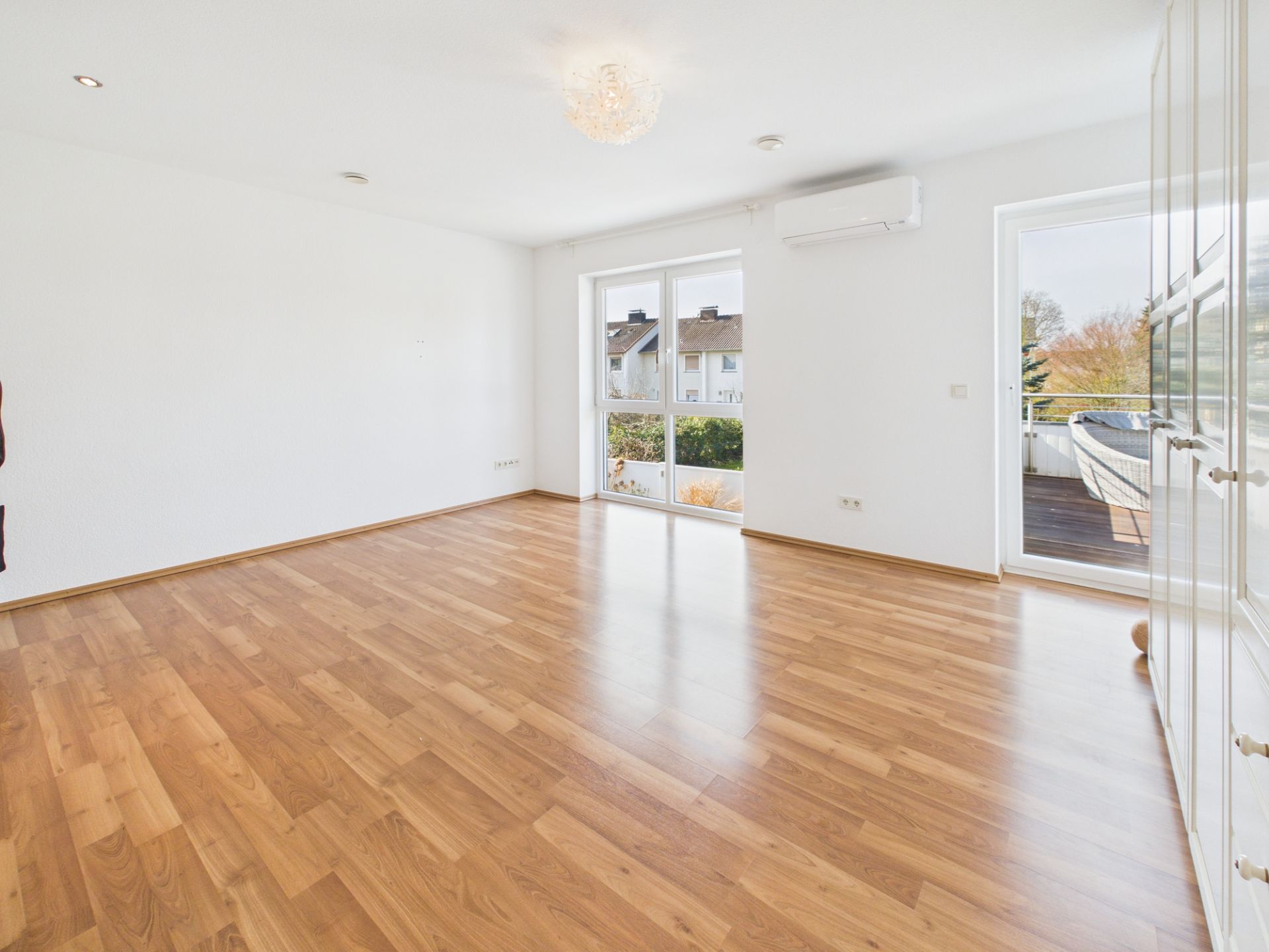 Helles, leeres Zimmer mit Parkettboden, weißen Wänden und Zugang zu einem Balkon.