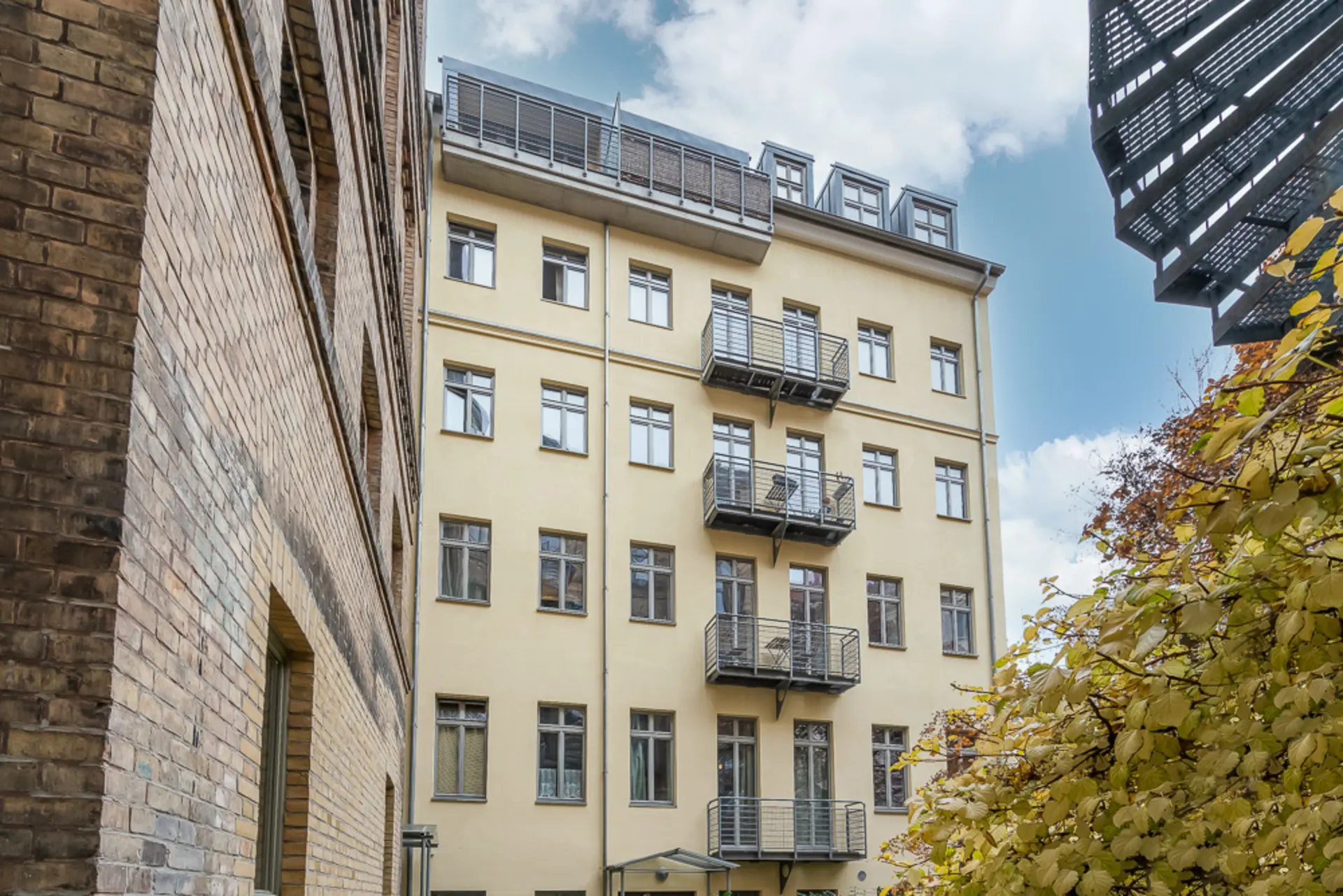 Mehrstöckiges Wohngebäude mit gelber Fassade und mehreren Balkonen, umgeben von Bäumen.